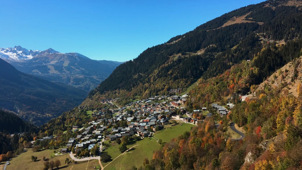 Champagny-en-Vanoise village nestled on a wooded valley slope with autumn colours and snow-capped peaks beyond